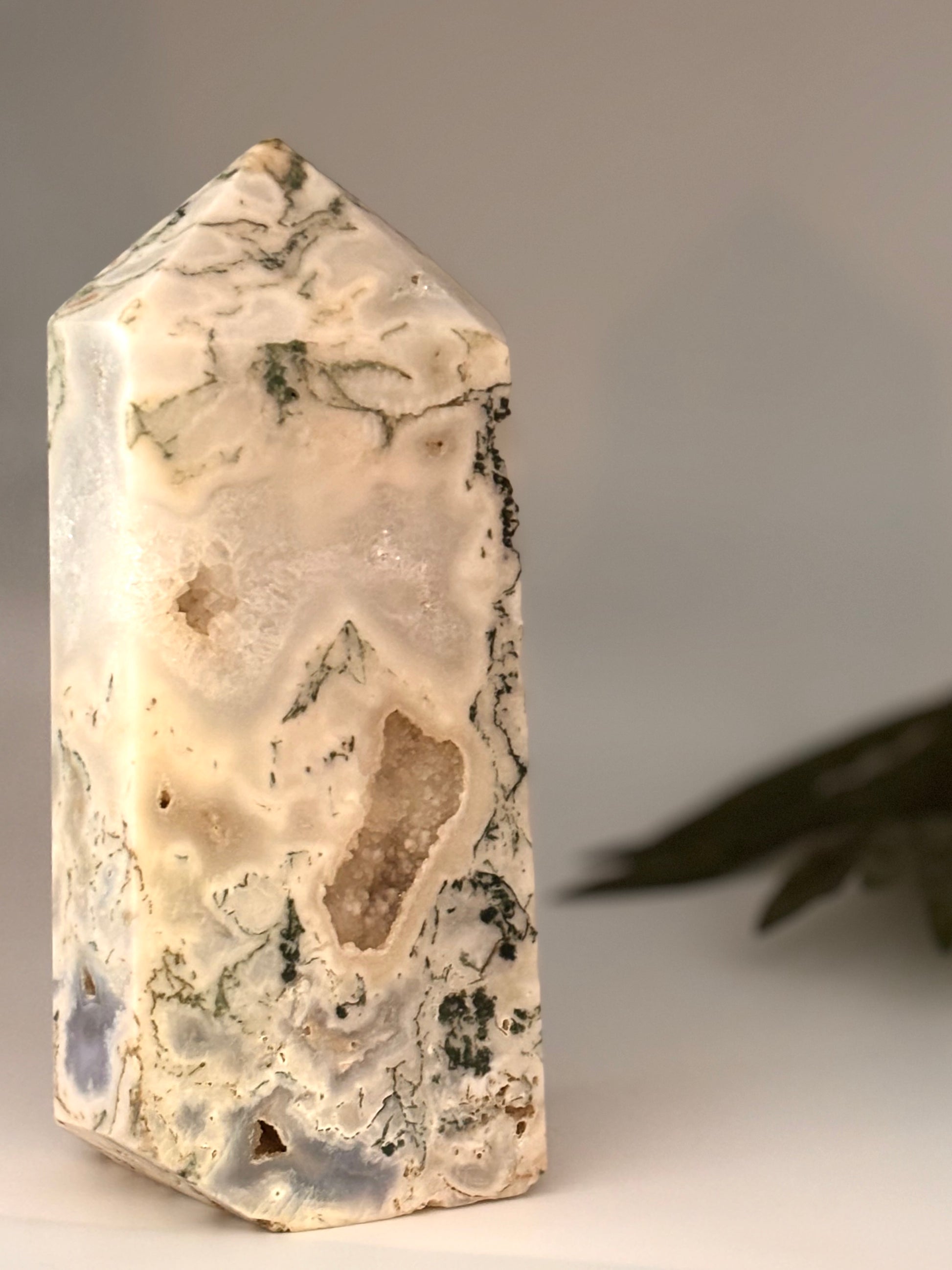 Decorative stone tower in green and white (moss Agate) with a leaf on a neutral background