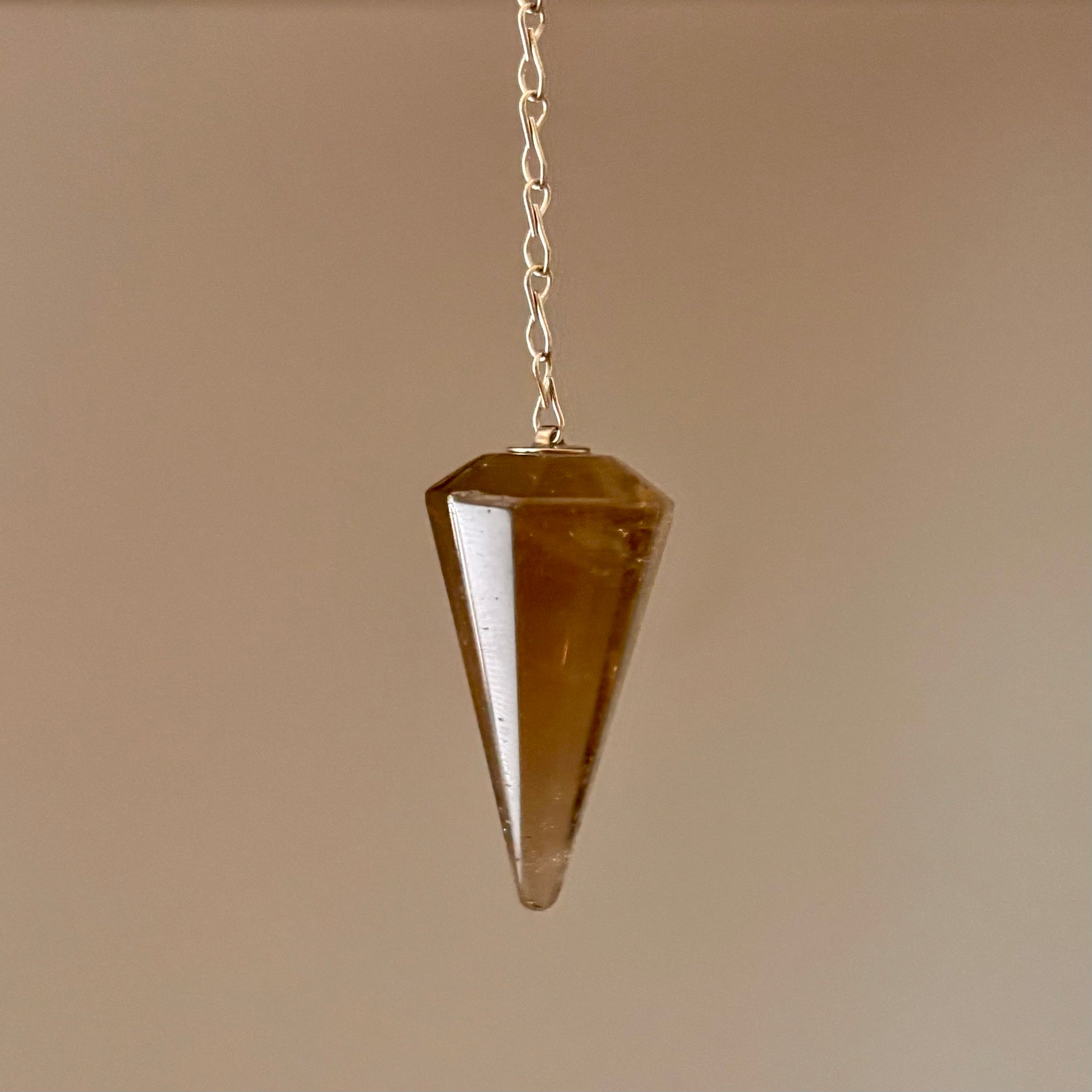 Brown crystal pendulum hanging on a chain against a beige backgroun