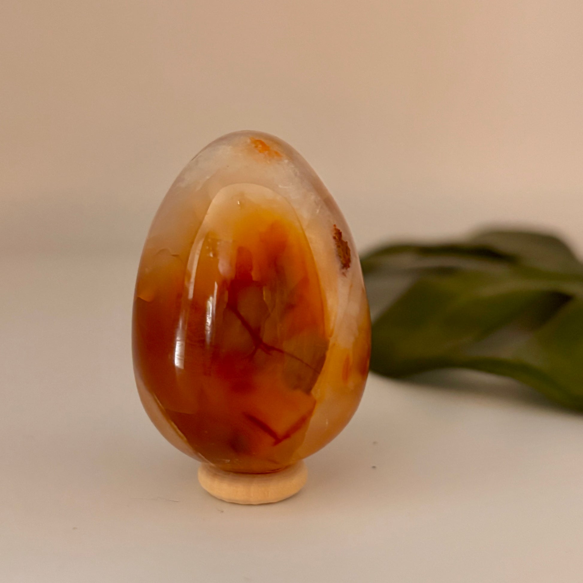 orange carnelian egg-shaped object on a beige surface with a green leaf in the background