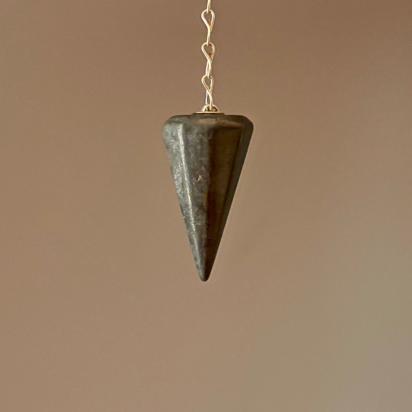 Grey pyrite  pendulum hanging against a cream background