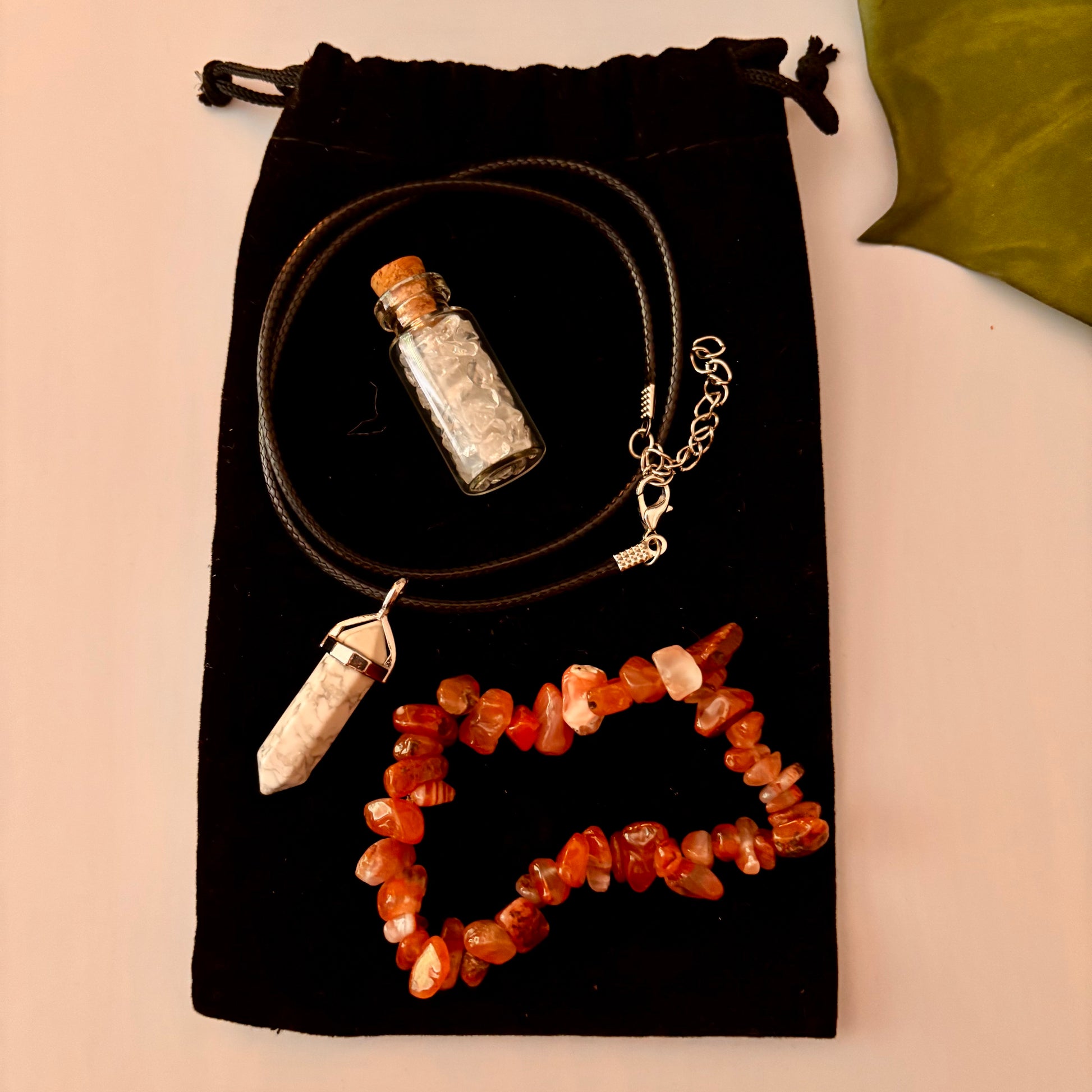 Necklace with a small bottle pendant, crystal necklace, and orange stone necklace on a black drawstring bag