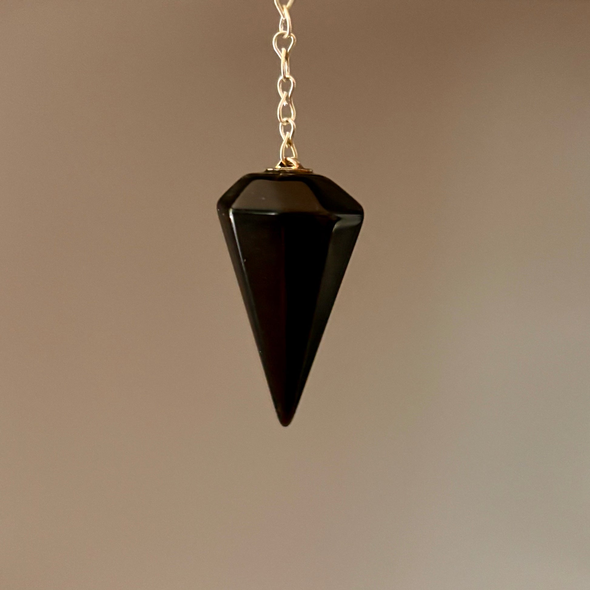 Black crystal pendulum on a silver coloured chain against a cream background
