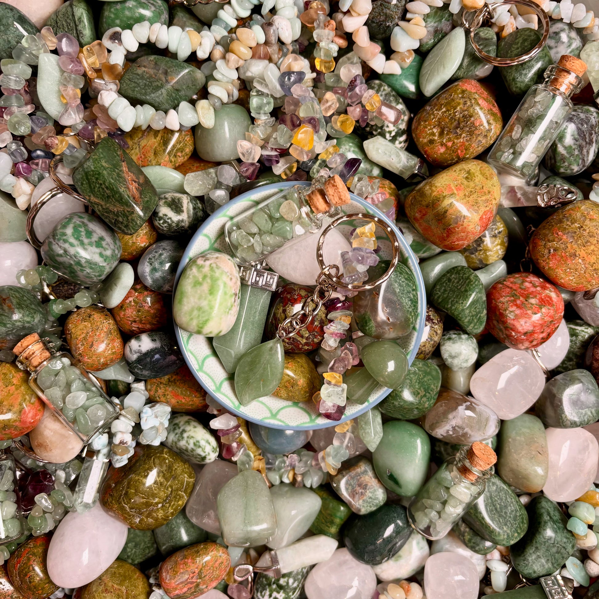Assorted green gemstones and jewelry in a bowl surrounded by more stones