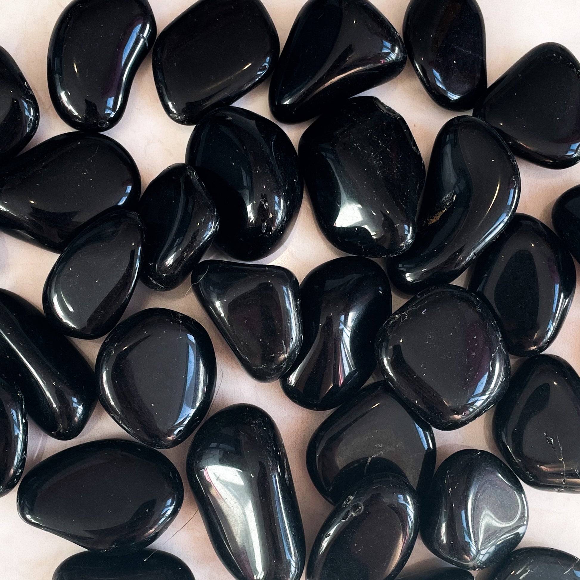 A collection of smooth, black obsidian stones with a glossy surface, arranged together.