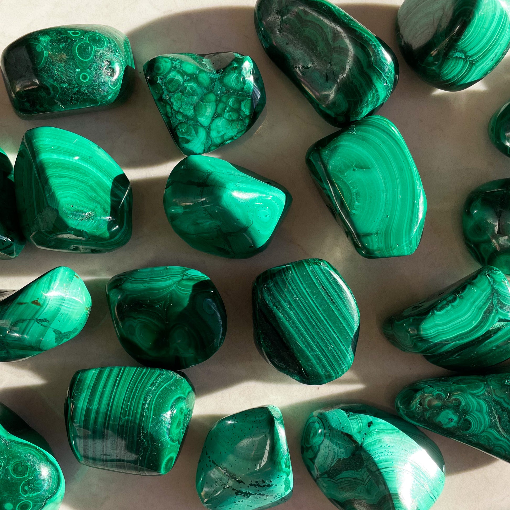 A collection of tumbled green Malachite crystals of various sizes.