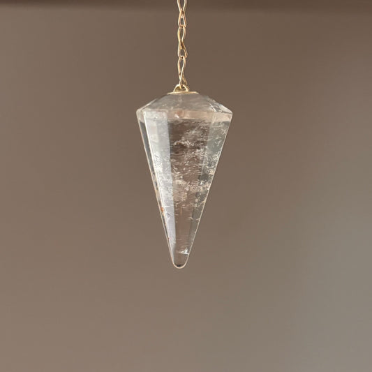 Clear quartz crystal pendulum on a chain against a cream background