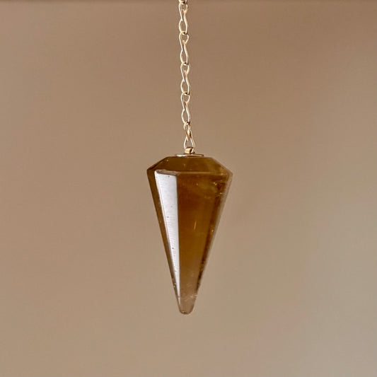Brown crystal pendulum hanging on a chain against a beige backgroun