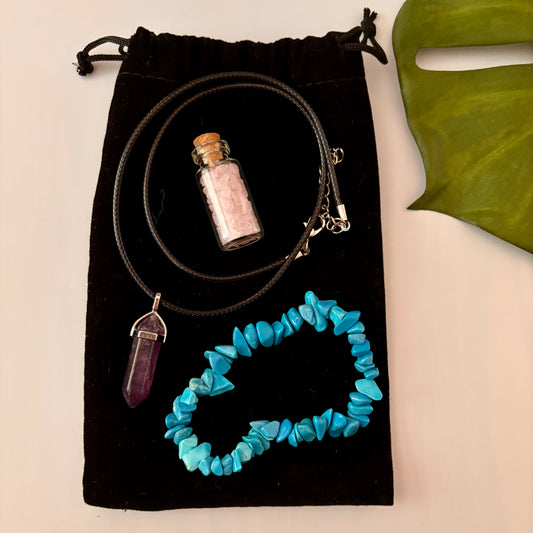 Black drawstring bag with jewellry including a blue beaded bracelet, pendant, and small bottle on a beige background.