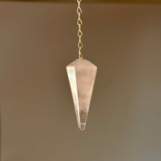 Crystal rose quartz pendulum hanging against a neutral background