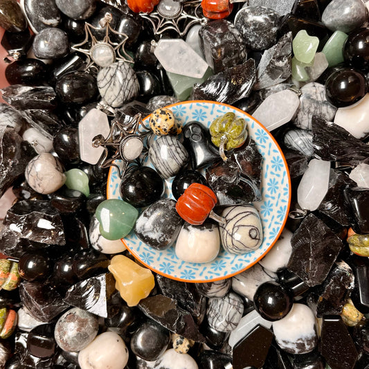 A scoop of deluxe Halloween crystal confetti containing various coloured gemstones and stones on a  plate.
