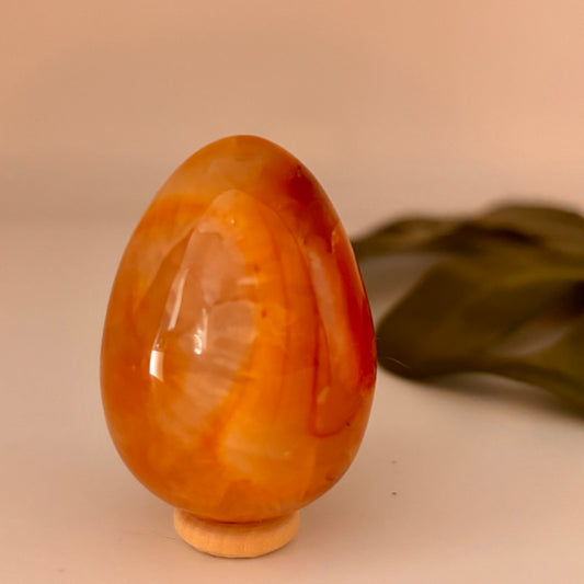 orange marbled egg-shaped object on a beige surface with a green leaf in the background