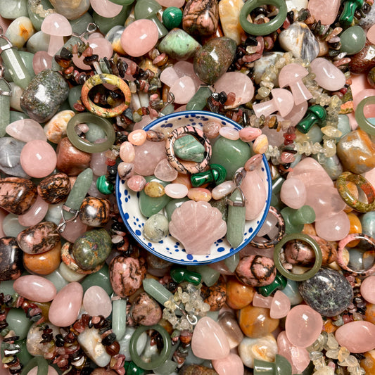 Assorted colourful in green and pink gemstones with a small bowl containing more stones.