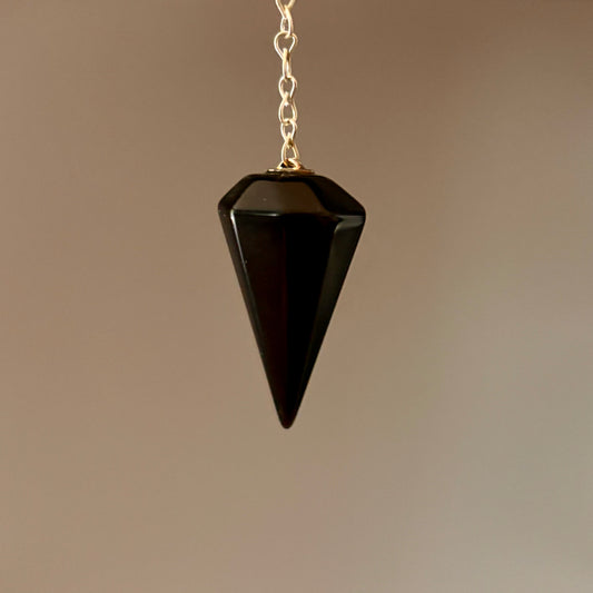 Black crystal pendulum on a silver coloured chain against a cream background