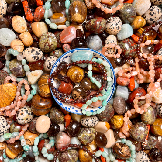 Assorted colourful beads and stones in red, orange and brown with a bowl of beads in the centre.