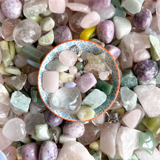 a collection of pastel coloured crystals including clear quartz, green aventurine, green jade and rose quartz in a little bowl