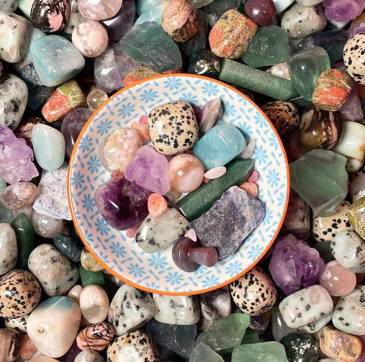a collection of crstals for spring including flower agate, leopardskin jasper, green aventurine and amethyst in a cute bowl