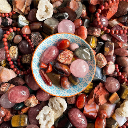 a collection of red crystals including red jasper, rose quartz, tigers eye and strawberry quartz in a little bowl.