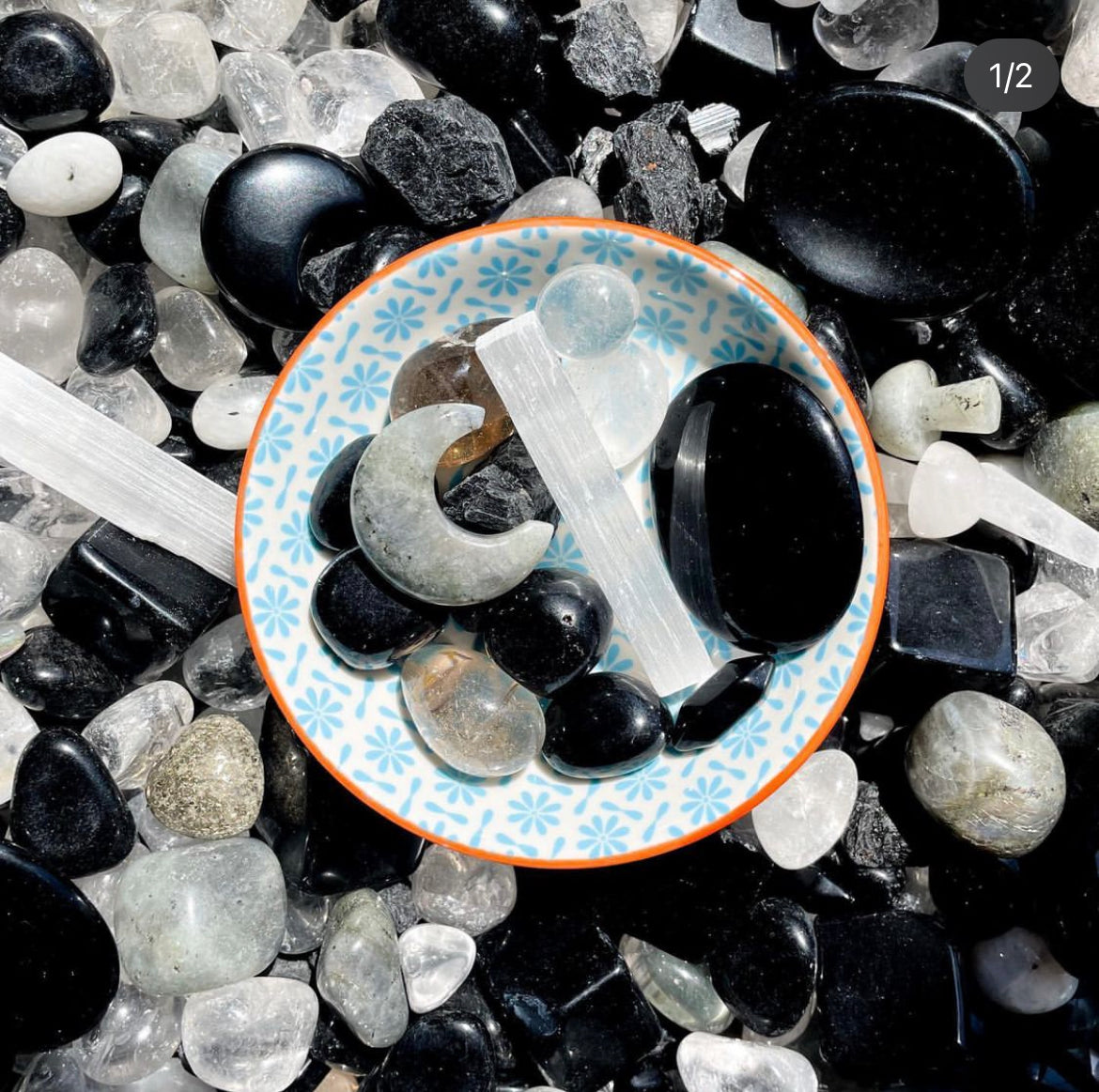 a collection of black, white and grey crystals in  bowl including black obsidian, clear quartz, selenite and labradorite