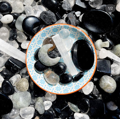 a collection of black, white and grey crystals in  bowl including black obsidian, clear quartz, selenite and labradorite