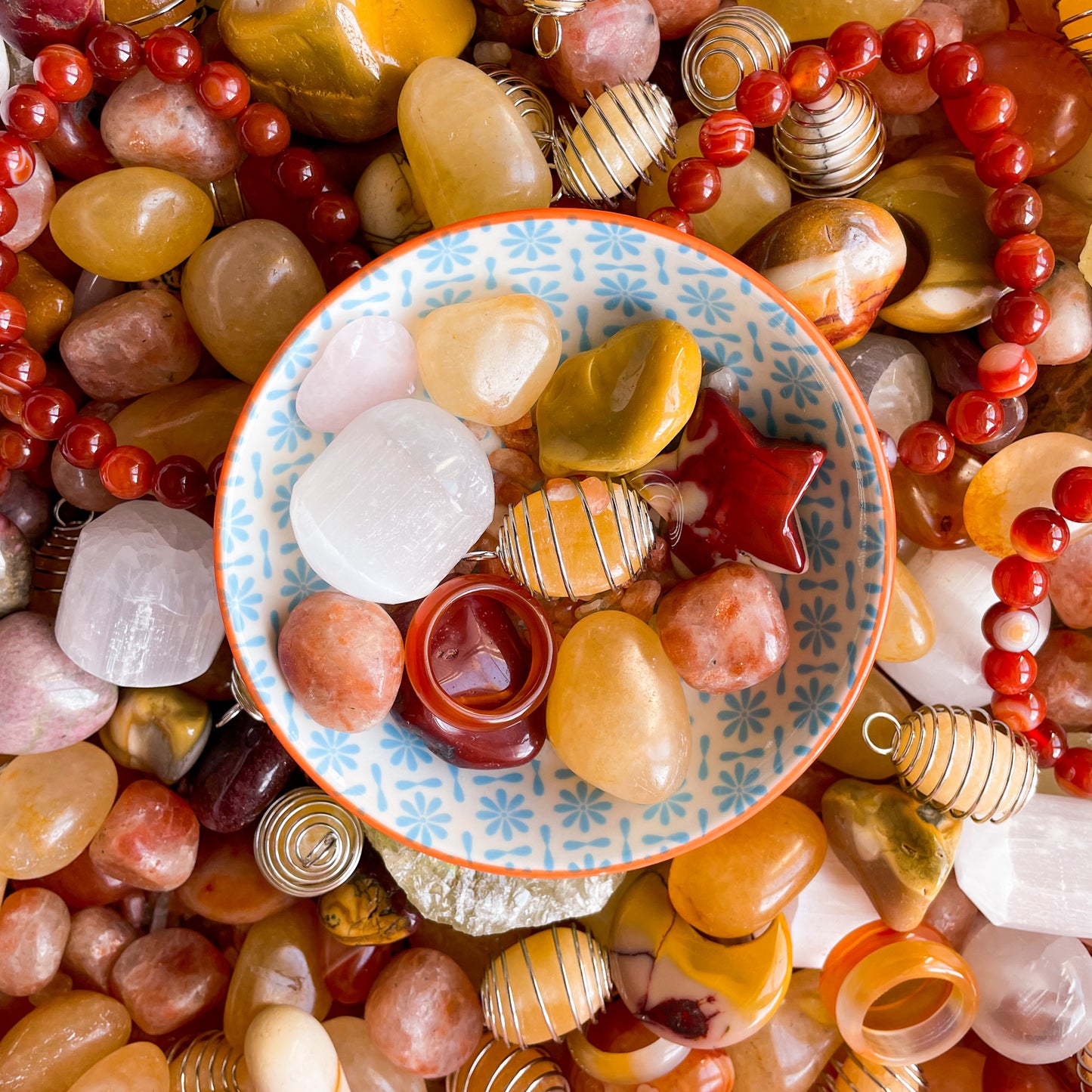 a collection of fire coloured crystals in a bowl with orange calcite, red jasper, carnelian and clear quartz